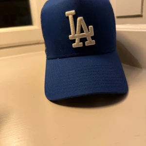Blå keps med LA-logga - Snygg blå keps från New Era med vit LA-logga framtill. Kepsen har ett mesh-tyg på sidorna och baksidan för extra ventilation. Perfekt för en avslappnad stil.