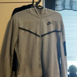 Grå hoodie från Nike - Säljer en grå hoodie från Nike med dragkedja och svart logotyp på bröstet. Den har långa ärmar och en stilren design med svarta detaljer. Perfekt för en avslappnad stil. Det står Xl+ i barn storlek men motsvarar S priset kan diskuteras 