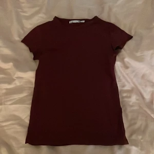 Mörkröd t-shirt från 157 - Säljer en stilren mörkröd t-shirt från 157. Den har en klassisk design med korta ärmar och rund halsringning. Perfekt för en avslappnad look. Den har dock ett litet hål på ryggen som knappt syns🌟