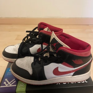 Nike Air Jordans i svart, vitt och rött - Säljer ett par klassiska Nike Air Jordans i svart, vitt och rött. Skorna har snörning och den ikoniska Air Jordan-loggan på sidan. Perfekta för sneaker-entusiaster.