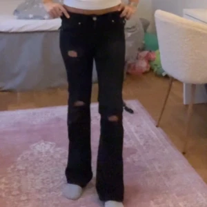 Svarta bootcut jeans med slitningar - Snygga svarta bootcut jeans med slitningar på knäna. Perfekta för en trendig look. De har en låg midja och klassisk femficksdesign. (Har gjort hålen själv)