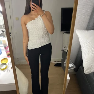 Vit axelbandslös topp - Säljer en söt vit axelbandslös topp med volangdetaljer. Toppen har en smockad design som ger en fin textur och passform. Perfekt för sommarens varma dagar.