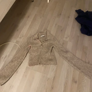 Beige ribbad kofta från Bershka - Säljer en snygg beige ribbad kofta från Bershka med knappar framtill. Koftan har långa ärmar och en klassisk krage, perfekt för lager-på-lager-stil.