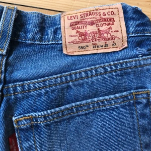 Levi's 550 Relaxed Fit Jeans - Säljer ett par klassiska blå Levi's 550 jeans med relaxed fit. De är tillverkade i 100% bomull och har en bekväm passform. Perfekta för en avslappnad stil.                                                   550tm, 14slim. Waist-25 Length-27