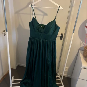 Grön långklänning från Hebeos - Elegant grön långklänning från Hebeos med smala axelband och v-ringad design. Klänningen har en dragkedja i ryggen, säljer denna klänning då jag beställde två stycken i olika storlekar så den är endast testat då den var för stor för mig. Perfekt för speciella tillfällen. Strl 44, pris kan diskuteras vid snabb affär 😊