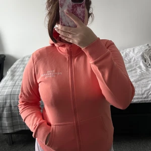 Korallfärgad hoodie från Peak Performance - Säljer en snygg korallfärgad hoodie från Peak Performance. Den har dragkedja framtill och långa ärmar. 