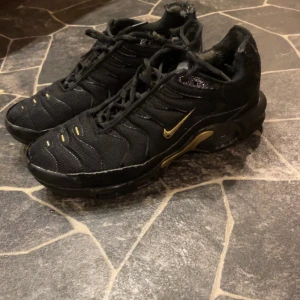 Svarta Nike sneakers med gulddetaljer - Snygga svarta Nike sneakers med gulddetaljer och snörning. Perfekta för en sportig look med en touch av stil. Skorna har en robust sula och är designade för komfort och hållbarhet. Nypris 2000 mitt pris 500