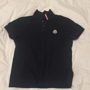 Navy blue  pikétröja från Moncler - Snygg blå pikétröja från Moncler med korta ärmar och klassisk krage. Tröjan har en broderad logotyp på bröstet och knappar framtill. Perfekt för en stilren look. Skriv för förhandling 