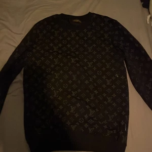 Svart tröja från Louis Vuitton - Snygg svart tröja från Louis Vuitton med deras ikoniska monogrammönster. Tröjan har långa ärmar och en rund halsringning. Perfekt för en stilren look.