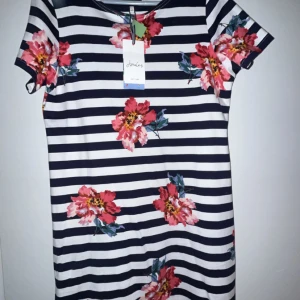 Randig blommig klänning från Joules - Säljer en snygg randig klänning från Joules med blommigt mönster i rosa och rött. Klänningen har korta ärmar och en bekväm passform. Perfekt för en somrig look! Nypris 55 euro vilket motsvarar cirka 635kr. Aldrig använd med etikett!