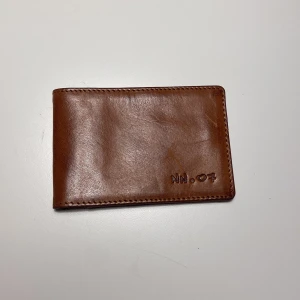 Brun plånbok från NN.07 - Snygg brun plånbok i skinn från NN.07. Den har en stilren design med plats för kort och ID. Perfekt för den som vill ha en klassisk och tidlös accessoar.