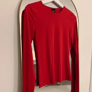 Röd långärmad topp från Gina Tricot - Snygg röd långärmad topp från Gina Tricot i ett mjukt och stretchigt material. Perfekt för att lägga till en färgklick i garderoben. Passar bra till både jeans och kjol. Tummhåll. Second skin känsla