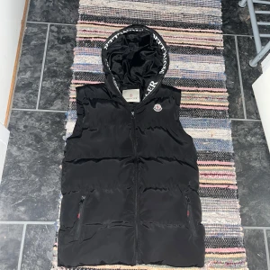 Moncler väst - Tjena! Säljer nu denhär sjukt feta moncler väst. Västen har Moncler-logga på bröstet och text på huvan. Perfekt för kyliga dagar när du vill hålla stilen. Passar nog dig som är runt 174-180cm lång.väldigt bra skick då de inte finns några skavanker eller skador! Priset är inte hugget i sten!