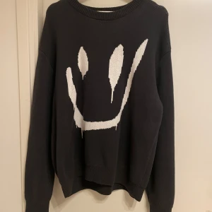 Svart tröja med smiley från Weekday - Säljer en svart tröja från Weekday med ett stort vitt smiley-motiv på framsidan. Tröjan har långa ärmar och en rund halsringning. Perfekt för en avslappnad stil.