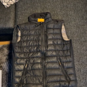 Pjs väst - Snygg svart dunväst med dragkedja och hög krage. Perfekt för kyligare dagar. Västen har praktiska fickor med dragkedja och en stilren design. Har ett litet hål vid högra fickan pris kan diskuteras. Barnstorlek L.