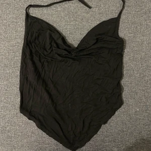 Svart axelbandslös topp - Snygg svart axelbandslös topp med knytband runt halsen. Perfekt för en kväll ute eller en somrig dag. Toppen har en elegant och enkel design.