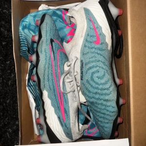 Nike phantom gx elite - Snygga Nike elite phantom gx fotbollsskor i blått med rosa detaljer och snörning. Skorna har en modern design med mönstrad yta och är perfekta för fotbollsplanen. Nypris 3800kr