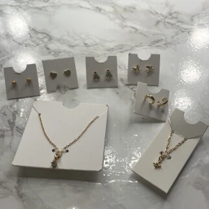 Set med guldiga smycken - Ett elegant set med guldiga smycken. Innehåller örhängen i form av hjärtan, julgranar och stjärnor, samt ett halsband med en stjärnberlock. Perfekt för att lägga till en glittrig touch till din outfit.70kr för allt!