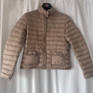 Beige dunjacka från J.O.T.T - Snygg beige dunjacka från J.O.T.T med dragkedja och hög krage i storlek XS, märken på knapparna (se bild) annars i väldigt fint skick🌸