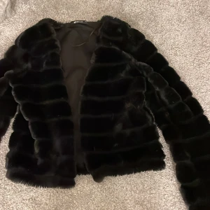 Svart pälsjacka - Snygg svart pälsjacka med långärmad design. Den är rätt så tunn så man kan ha den till våren eller tidigt på hösten. Jackan har en elegant look och passar bra till olika tillfällen.