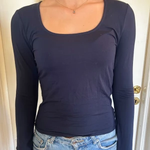 Svart långärmad topp - Säljer en stilren marinblå långärmad topp med en urringning. Tröjan är tight och perfekt för olika tillfällen. Materialet är mjukt och stretchigt, vilket gör den superbekväm att ha på sig. Ärmarna har en liten volangdetalj vid slutet för en extra touch av stil. Köpt från Ginatricot softtouch serien.