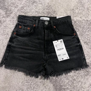 Jeansshorts  - Säljer ett par snygga mörkgråa shorts från Zara i storlek 32. Shortsen är i nyskick och har även prislappen kvar. Pga den neutrala färgen är det lätt att matcha shortsen med alla möjliga plagg och färger!