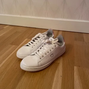 Vita sneakers med hjärtdetalj - Säljer ett par vita sneakers med en söt stjärndetalj  på sidan. Skorna har snörning och en klassisk design som passar perfekt till vardags. De är i bra skick och redo för nya äventyr!