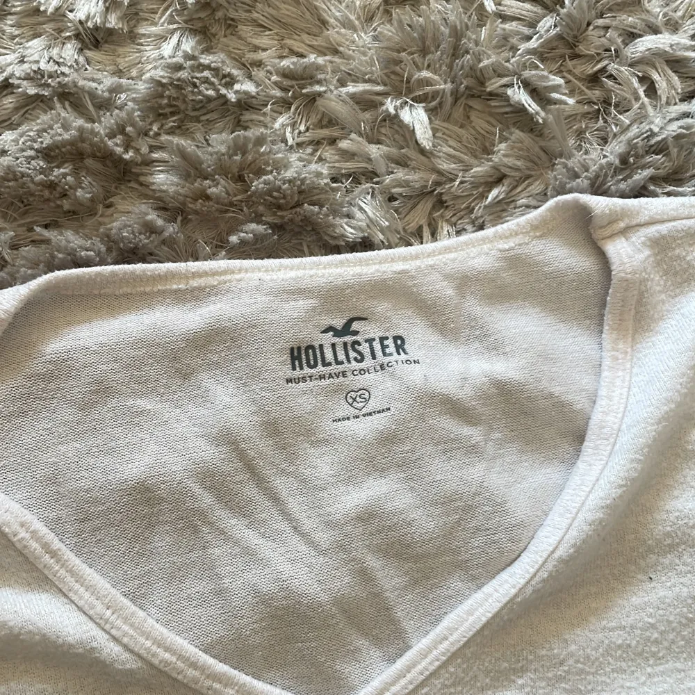 Säljer en enkel och stilren vit t-shirt från Hollister. Den har en v-ringad hals och korta ärmar, perfekt för en avslappnad look. Materialet känns mjukt och bekvämt, idealiskt för vardagsbruk.. T-shirts.