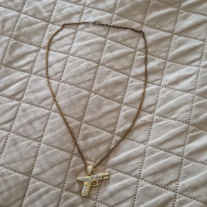 Guldhalsband med pistolhänge - Säljer ett coolt guldhalsband med ett pistolformat hänge. Hänget är dekorerat med glittrande stenar som ger en extra bling-effekt. Perfekt för att sticka ut på festen eller bara för att lägga till lite edge till din outfit.