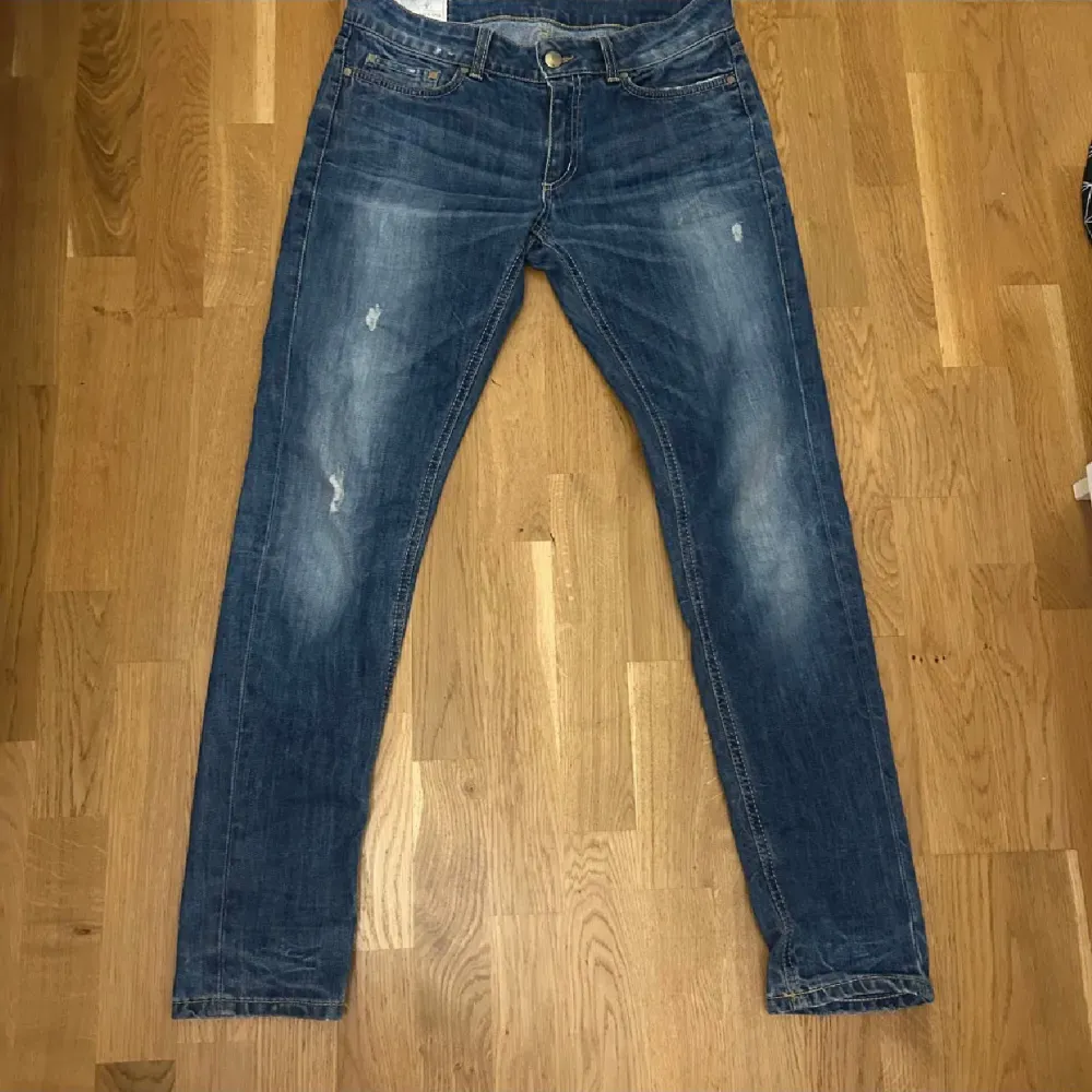 Säljer ett par snygga blå jeans med coola slitningar. De har en klassisk femficksdesign och en knappgylf. Perfekta för en avslappnad stil och passar till det mesta i garderoben.. Jeans & Byxor.