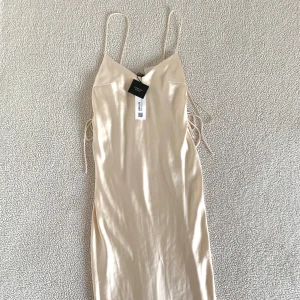 ZARA elegant krämvit satinklänning med snörningar - Otroligt vacker och elegant krämvit satinklänning i midilängd från ZARAs festive kollektion. Öppen på sidorna med snörningar. Ny med prislappar. Ordinariepris 659kr. 