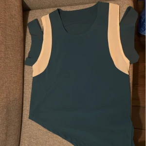 Blå ärmlös topp med beige detaljer - Säljer en snygg blå open shoulder topp, assymetrisk med beige detaljer. Perfekt för sommardagar eller som ett lager under en jacka. Toppen har en enkel och stilren design som passar till det mesta. Skön och lätt att bära!