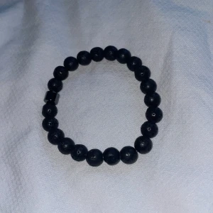 Svart pärlarmband - Snyggt svart armband med runda pärlor, perfekt för både vardag och fest. Pärlorna har en matt finish och en unik textur som ger en cool look. Armbandet är elastiskt och passar de flesta handleder. En stilren accessoar som enkelt kan matchas med andra smycken.