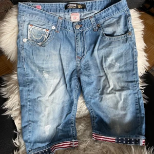 True Religion Jeansshorts Unisex  - True Religion jeansshorts i nyskick. Använda ett fåtal gånger utan defekter. Storlek: 36” Midjemått: 90 (cm) Material: Bomull De har en gulnad lite halv ”smutsig” look som får varan att se väldigt vintage ut.