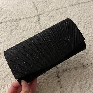 Svart väska  - Säljer denna snygga svarta glittriga väska. Den är aldrig använd. Perfekt som väska till balen eller liknande