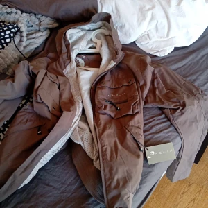Brun jacka från Phelix - Säljer en brun jacka från Phelix i storlek S. Den har en cool design med dragkedja och knappar, samt en huva för extra skydd. Perfekt för kyliga dagar med sin funktionella stil och Arctic Ocean-märke på insidan. Jackan är i bra skick och redo för nya äventyr!
