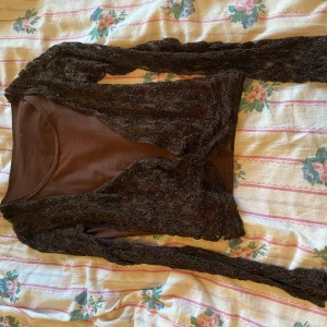 Brun topp med spetsdetaljer - Säljer en snygg brun topp med långa ärmar och spetsdetaljer. Perfekt för höst och vår, den har en normal passform och är gjord i ett mjukt material. Toppen är i nyskick och passar både till vardags och fest. Perfekt för dig som vill ha något unikt i garderoben!