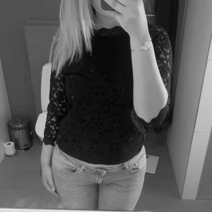 Svart spetsblus - Säljer en elegant svart spetsblus med trekvartsärmar. Perfekt för en kväll ute eller en fest. Blusen har ett vackert blommönster och är i nyskick. Passar bra till både jeans och kjol!