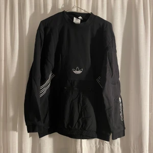 Svart tröja från Adidas - Säljer en snygg svart tröja från Adidas med deras klassiska logga på bröstet och ärmen. Tröjan har långa ärmar och är perfekt för både vardag och träning. Den är i bra skick och superbekväm att ha på sig. Passar perfekt till höst och vinter!