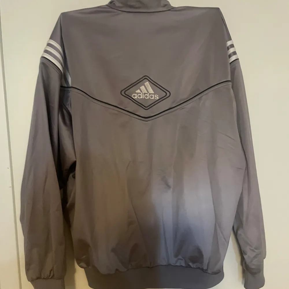 Säljer en grå träningsjacka från Adidas i storlek M. Perfekt för träning eller som en casual vardagskofta. Har användts ett fåtal gånger. Är i ok skick då den är vintage.. Tröjor & Koftor.