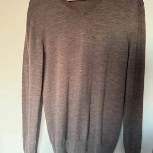 Grå tröja i merinoull från John Henric - Säljer en stilren grå tröja från John Henric i 100% merinoull. Tröjan har en v-ringad design och långa ärmar, perfekt för kyligare dagar. Den är mjuk och bekväm, vilket gör den till ett utmärkt val för både vardag och mer uppklädda tillfällen. Säljer den då den är för liten, mycket bra skick då den är knappt använd, storlek M