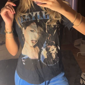 Svart t-shirt med tryck - Cool svart t-shirt med stort tryck av en artist på framsidan. T-shirten har en avslappnad passform och korta ärmar, perfekt för en casual look. Texten ovanför trycket är i blått och vitt.