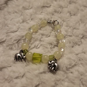Armband med elefantberlocker - Charmigt armband med vita och gröna pärlor samt två elefantberlocker i silverfärg. Pärlorna är runda och kubformade, vilket ger en lekfull och unik design. Perfekt för att lägga till en personlig touch till din stil.