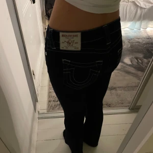 Svarta bootcut jeans från True Religion - Säljer ett par svarta bootcut jeans från True Religion, modell Becca. De har en midwaist passform och är dekorerade med kontrasterande sömmar. Perfekta för en stilren look. Knappt använda men har dock sytt som lite mer lowwaist vilket har gett lite defekt men inget som märks när man har jeansen på sig  köpta för 1600kr om jag minns rätt så säljer för väldigt bra pris 