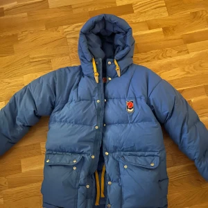 Blå dunjacka från Fjällräven - Säljer en blå dunjacka från Fjällräven. Bästa jackan för kalla dagar med sin varma vaddering och praktiska dubbelfickor på vardera sida. Denna jackan är retro, då den tillhör första släppet av just denna modellen, men den har varit inplastad och förvarad i en garderob och endast jag har använt den i en säsong 🫶🏼 Jag skulle säga att jackan passar XS/ S/ M, beroende på! Jag är 163 lång och vanligtvis XS, men den passar även min mamma som är 168 lång/ M.