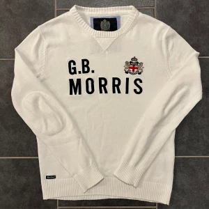 Vit tröja från Morris - Säljer en stilren vit tröja från Morris med texten 'G.B. MORRIS' och ett emblem på bröstet. Tröjan har långa ärmar och ribbade muddar. Perfekt för en klassisk look. (Sitter mer som en ”S”)