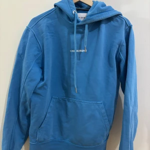 Blå hoodie från Calvin Klein Jeans - Säljer en snygg blå hoodie från Calvin Klein Jeans. Den har en klassisk design med känguruficka och justerbar huva med dragsko. Perfekt för en avslappnad stil. Nypris 1300
