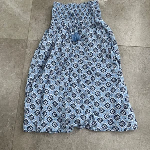 Mönstrad klänning/ kjol i blå toner - Charmig klänning/kjol med ett vackert mönster i olika blå toner. Klänningen/kjolen har en smockad överdel och knytband med tofsar i midjan. Perfekt för en avslappnad sommarlook.