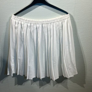 Vit plisserad kjol - Snygg vit plisserad kjol med knappar på sidan. Perfekt för en stilren look. Den elastiska midjan gör den bekväm att bära hela dagen. Väldigt genomskinlig.