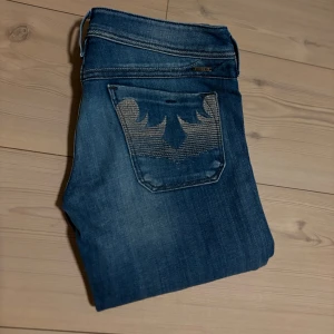 Blå jeans från Diesel - Snygga blå jeans från Diesel med broderade detaljer på bakfickorna. De har en klassisk femficksdesign och en knappgylf. Perfekta för en avslappnad stil.